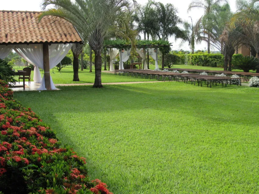 Quiosque de telhado de barro no gramado com canteiros floridos