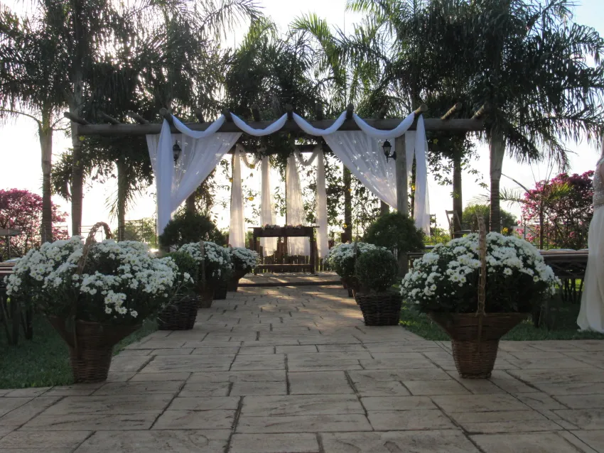 Altar de cerimônia ao ar livre com cortinas brancas e vasos de flores
