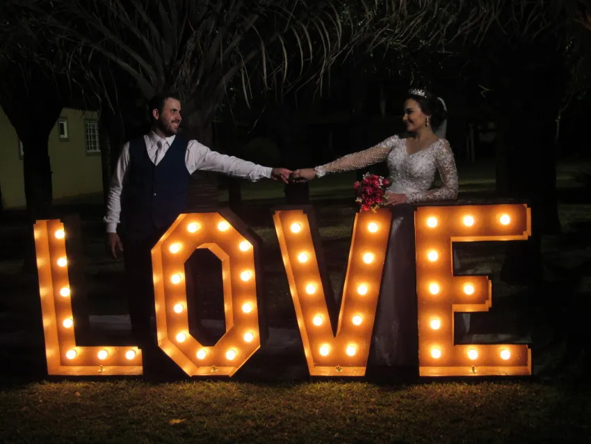Casal diante do letreiro iluminado “LOVE” à noite
