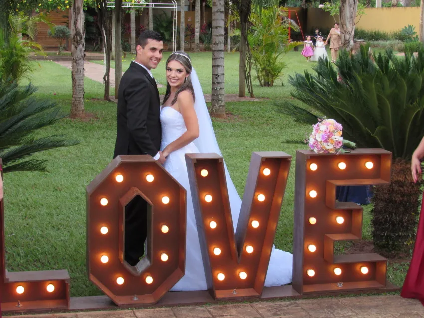 Casal de noivos ao lado do letreiro “LOVE” no jardim