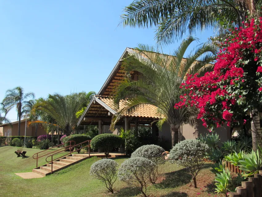 Fachada da sede com telhado de barro, jardim e árvores floridas
