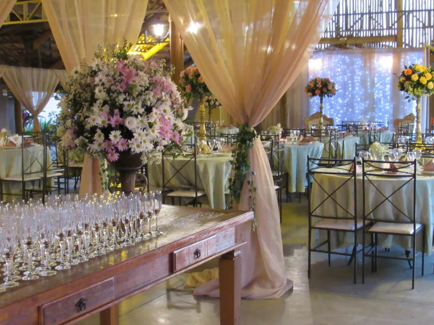 Salão com cortinas claras, mesas redondas e arranjos de flores