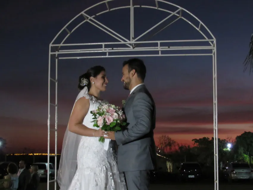 Casal de noivos sob arco metálico no fim da tarde